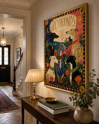 Decorative wall art of greyhounds in a home interior with a lamp and books on a table.