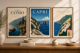 Three framed posters of Lake Como, Capri, and Amalfi on a wall above a wooden shelf.